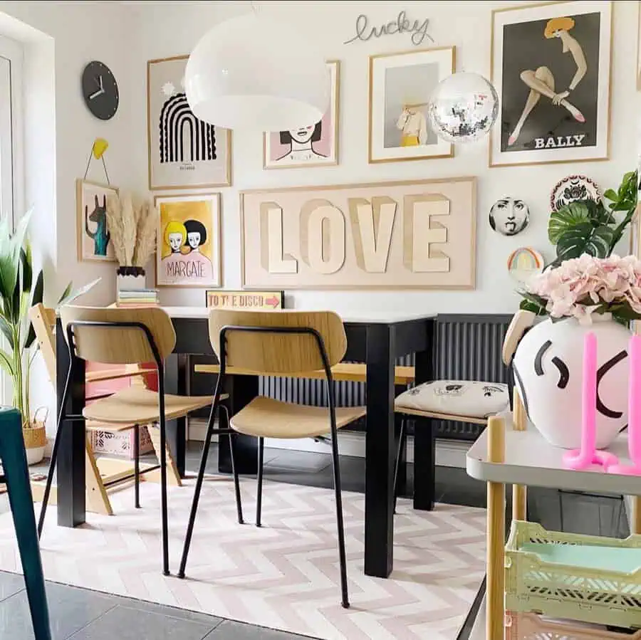 Colorful gallery wall with modern art pieces, a large "LOVE" sign, and fun decor elements in a vibrant dining room setup with black table and light wood chairs.