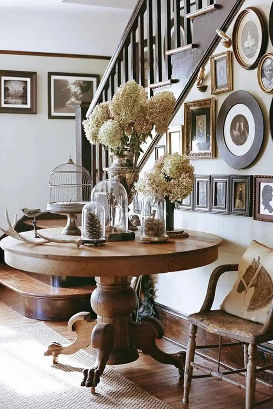 Rustic farmhouse entryway with vintage gallery wall, wooden table, and decorative glass cloches.