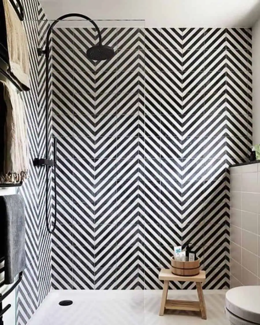 Black and white chevron-tiled shower with black fixtures and wooden stool for bath products.