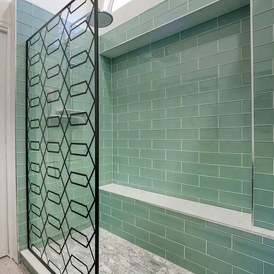 Mint green subway-tiled shower with geometric black metal divider and built-in bench.