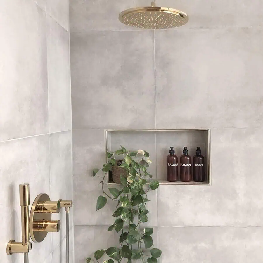 Luxurious shower with gold fixtures and a cascading golden pothos plant on a recessed shelf.