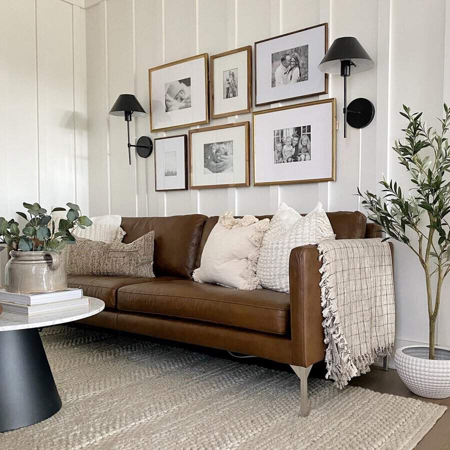 Farmhouse living room with a leather sofa, gallery wall, cozy pillows, and greenery.
