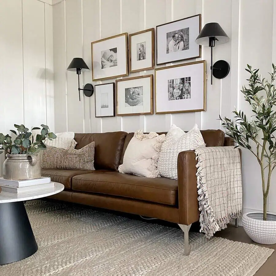 Farmhouse living room with a leather sofa, gallery wall, cozy pillows, and greenery.