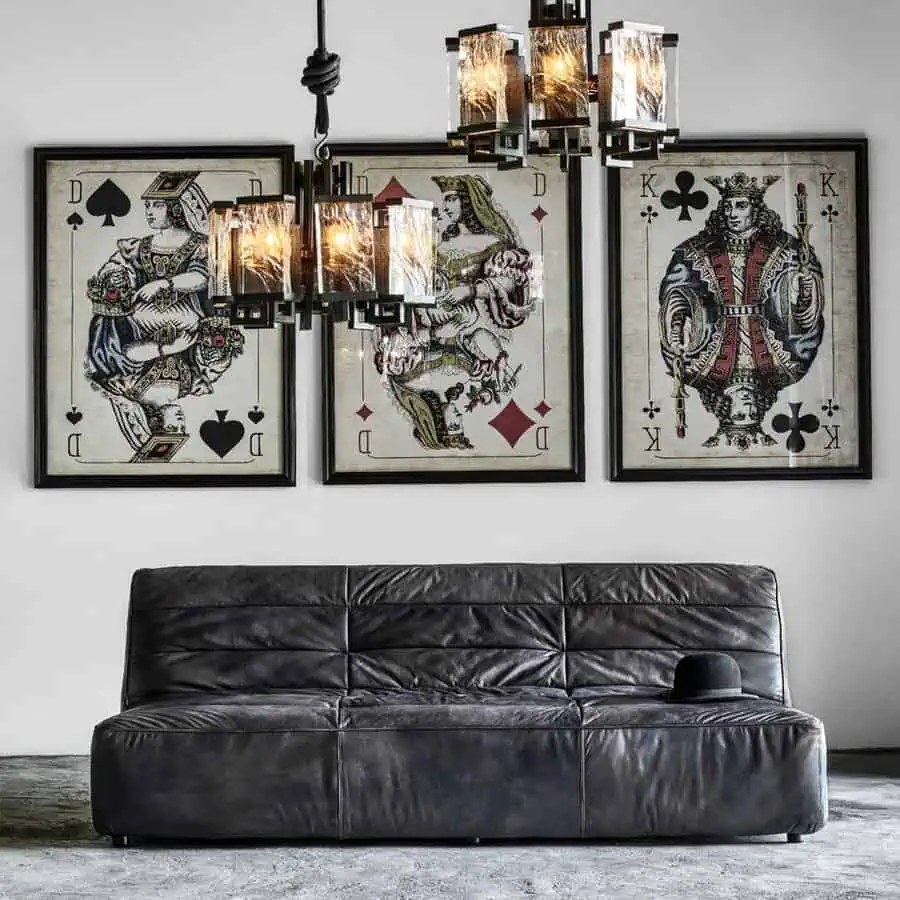 Industrial living room with a black leather sofa, oversized playing card artwork, and modern chandelier.