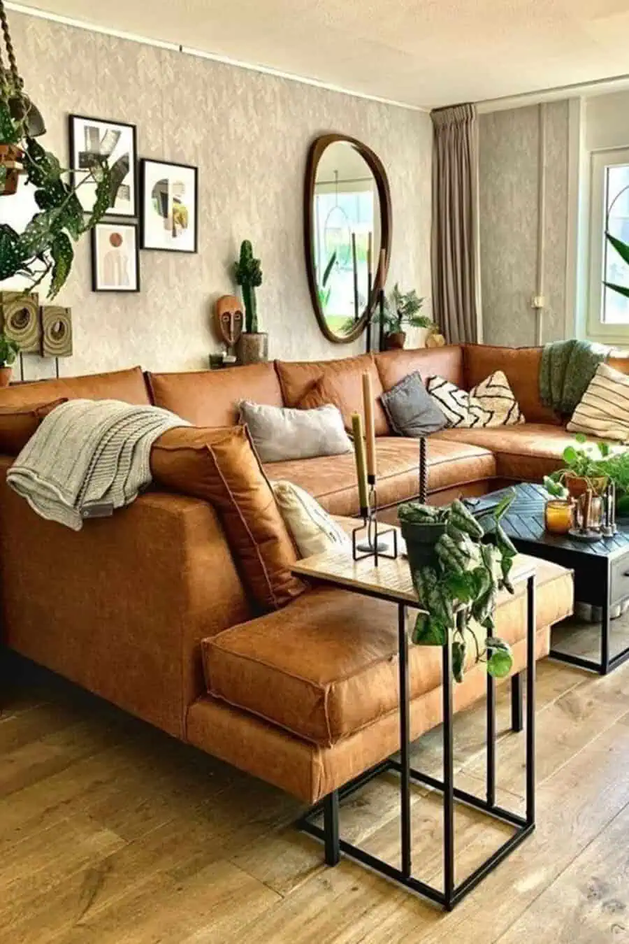 Large leather sectional in a rustic living room with plants, wall art, and a round mirror.