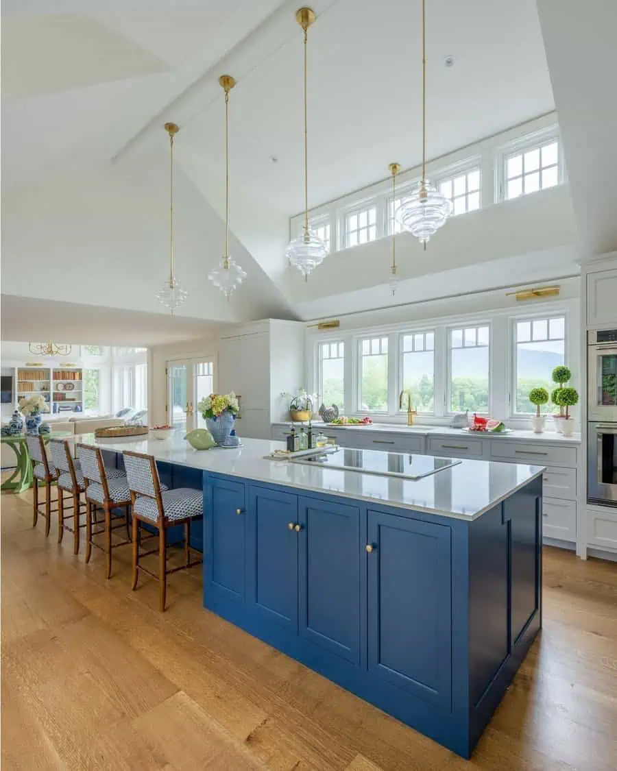 A bright kitchen with a bold blue island, pendant lights, and large windows that let in natural light.