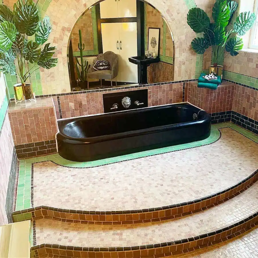 Art Deco bathroom with black bathtub, tiled steps, tropical plants, and curved walls.