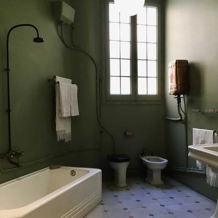 Minimalist Art Deco bathroom with olive green walls, vintage bathtub, and geometric tile flooring.