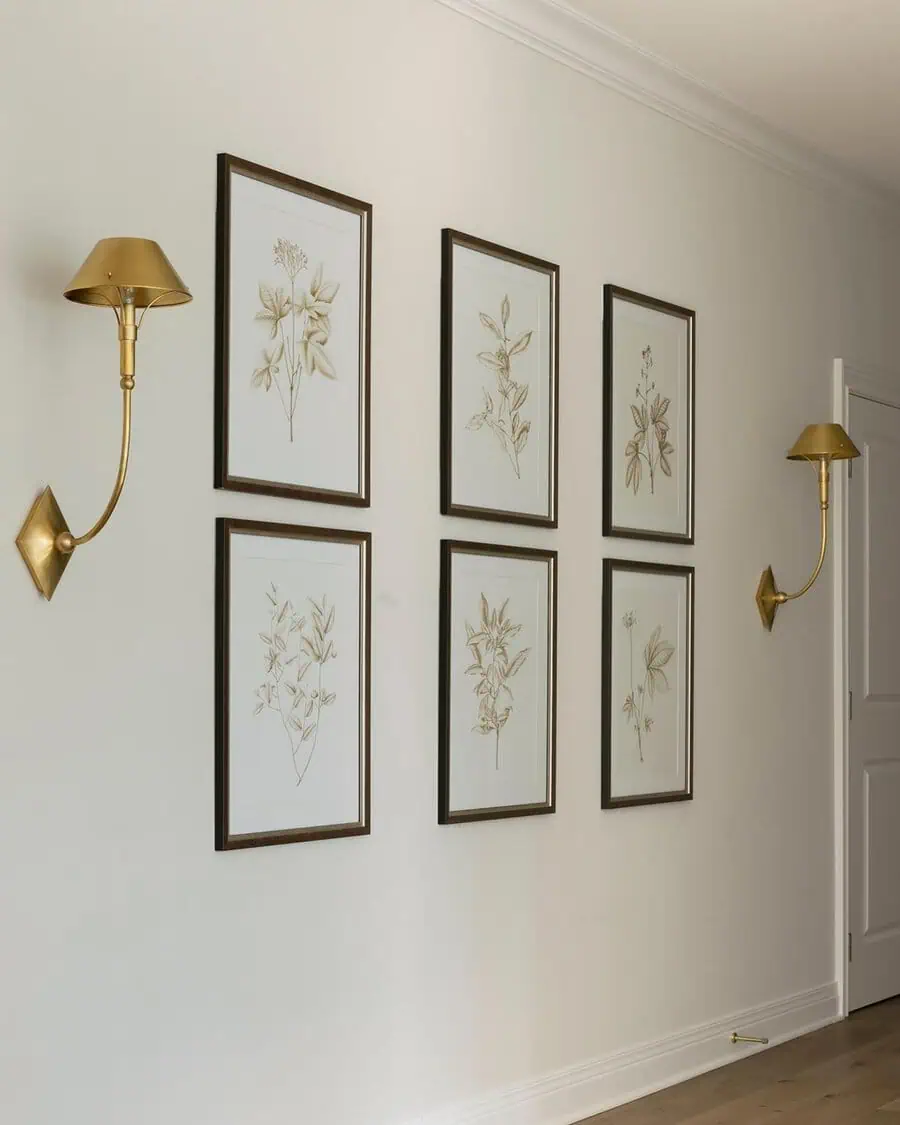 Minimalist hallway with botanical prints and brass sconces on neutral-colored walls.