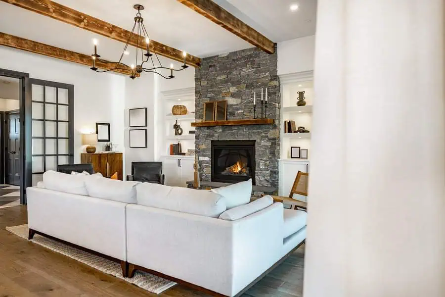 Modern fireplace with a stone facade, wooden mantel, and stylish seating arrangement.