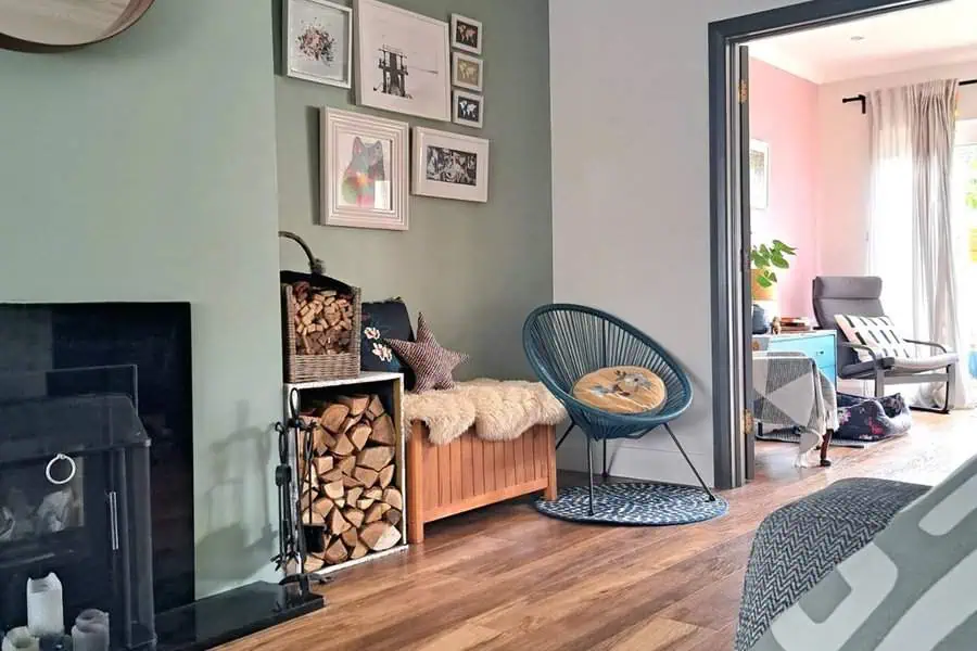 Cozy nook with wood storage, wall art, and a blue chair beside a fireplace in a modern living room.