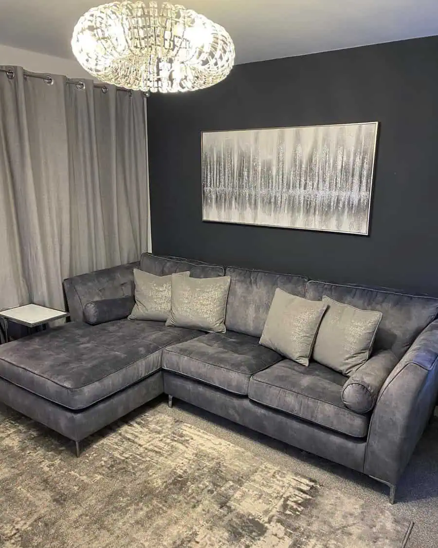 Modern living room with a grey sectional sofa, dark accent wall, abstract artwork, and crystal chandelier.