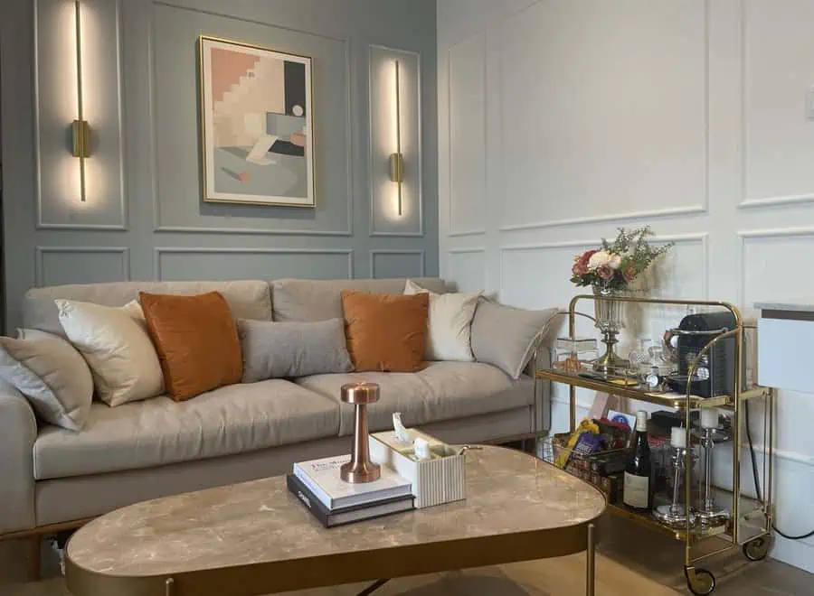 Stylish living room with a beige sofa, orange pillows, modern wall sconces, and a gold bar cart.