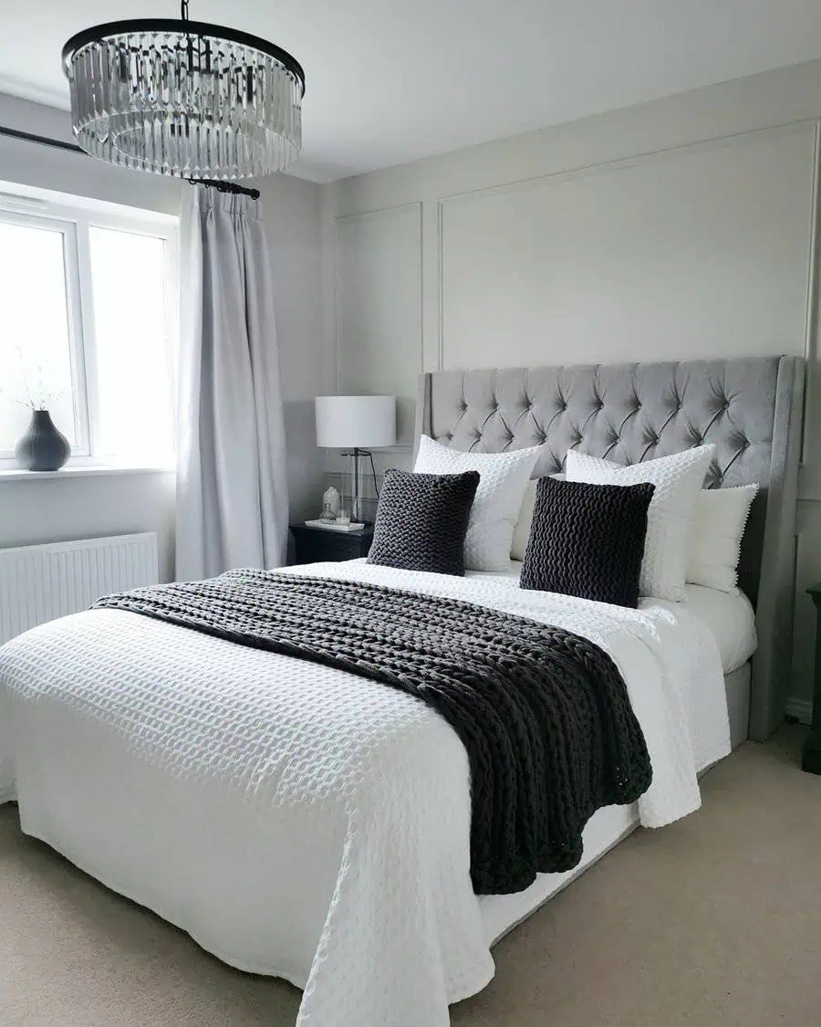 Modern bedroom with a grey tufted headboard, white bedding, black accent pillows, and a crystal chandelier.