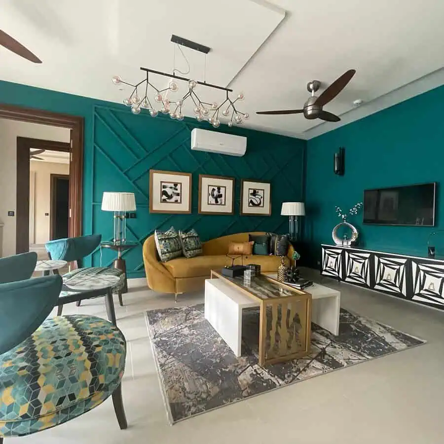 Vibrant living room with teal walls, mustard sectional, geometric decor, and a modern chandelier.