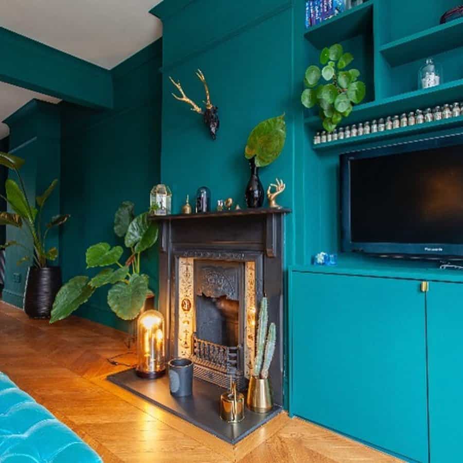 Bold living room with teal walls, dark fireplace, indoor plants, and wooden floors.