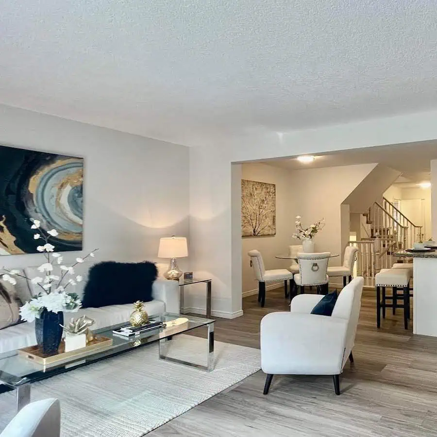 Bright open-concept living and dining room with white furniture, modern art, and wood floors.