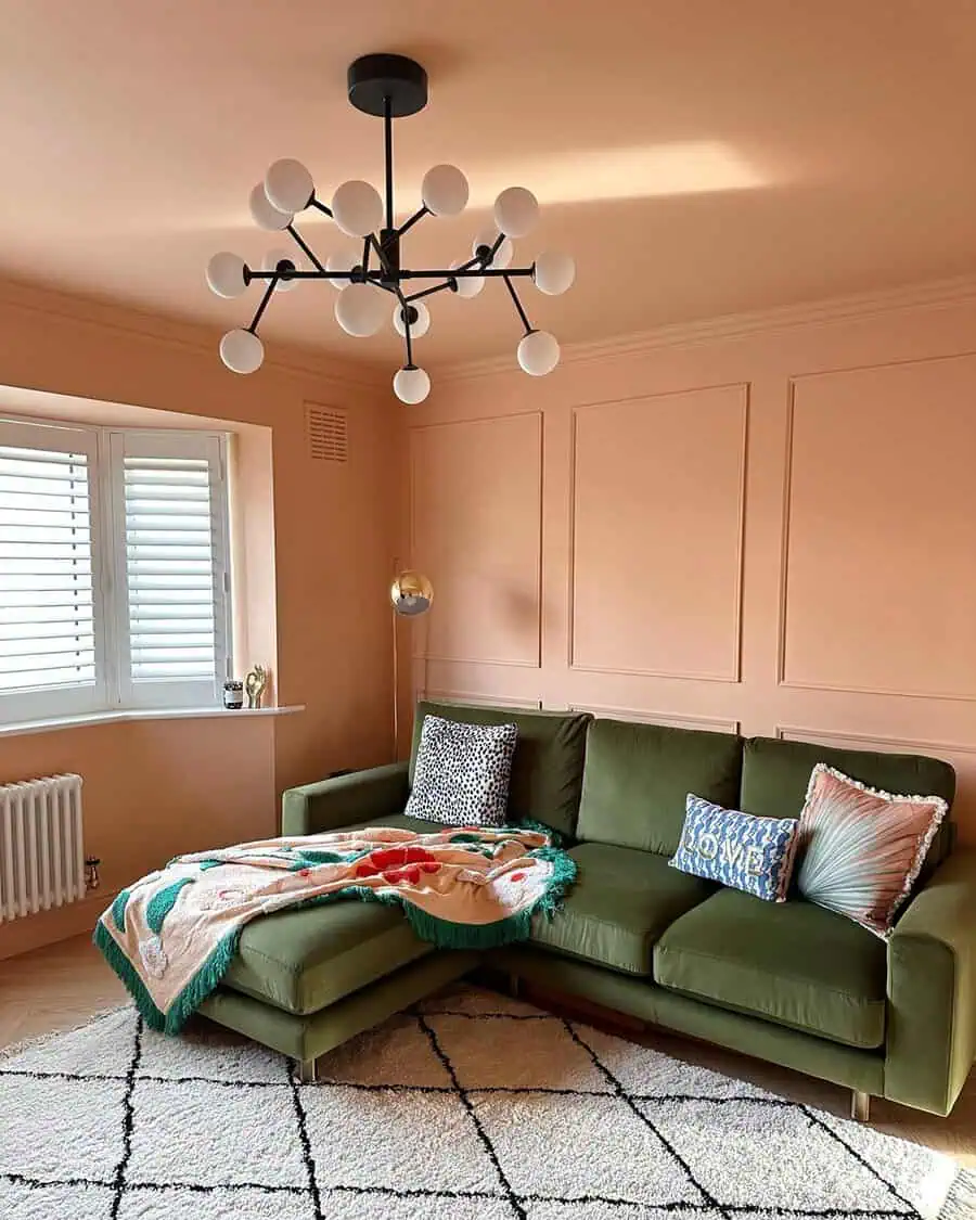 Living room with peach-colored walls, green velvet sofa, modern chandelier, and cozy decor accents.