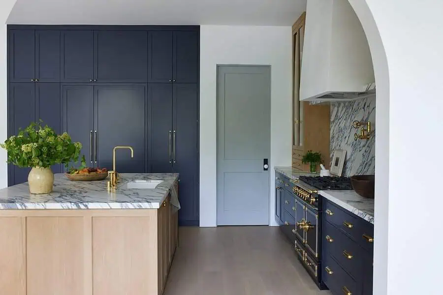 Modern kitchen with navy cabinets, marble countertops, gold accents, and a wooden island.