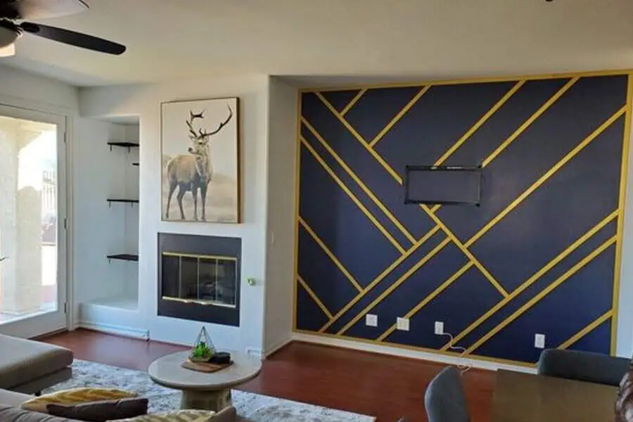 Living room featuring a bold navy accent wall with gold geometric lines, a fireplace with a deer painting above it, and minimalist decor.