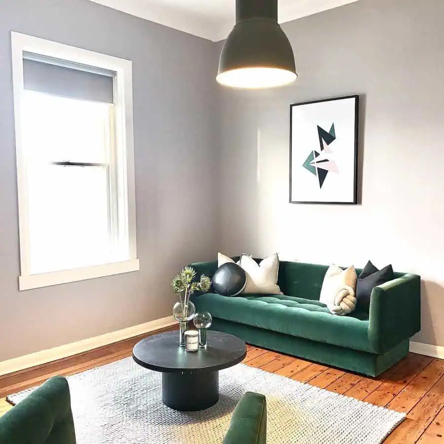 Minimalist living room with a green sofa, modern art, round black coffee table, and grey walls.