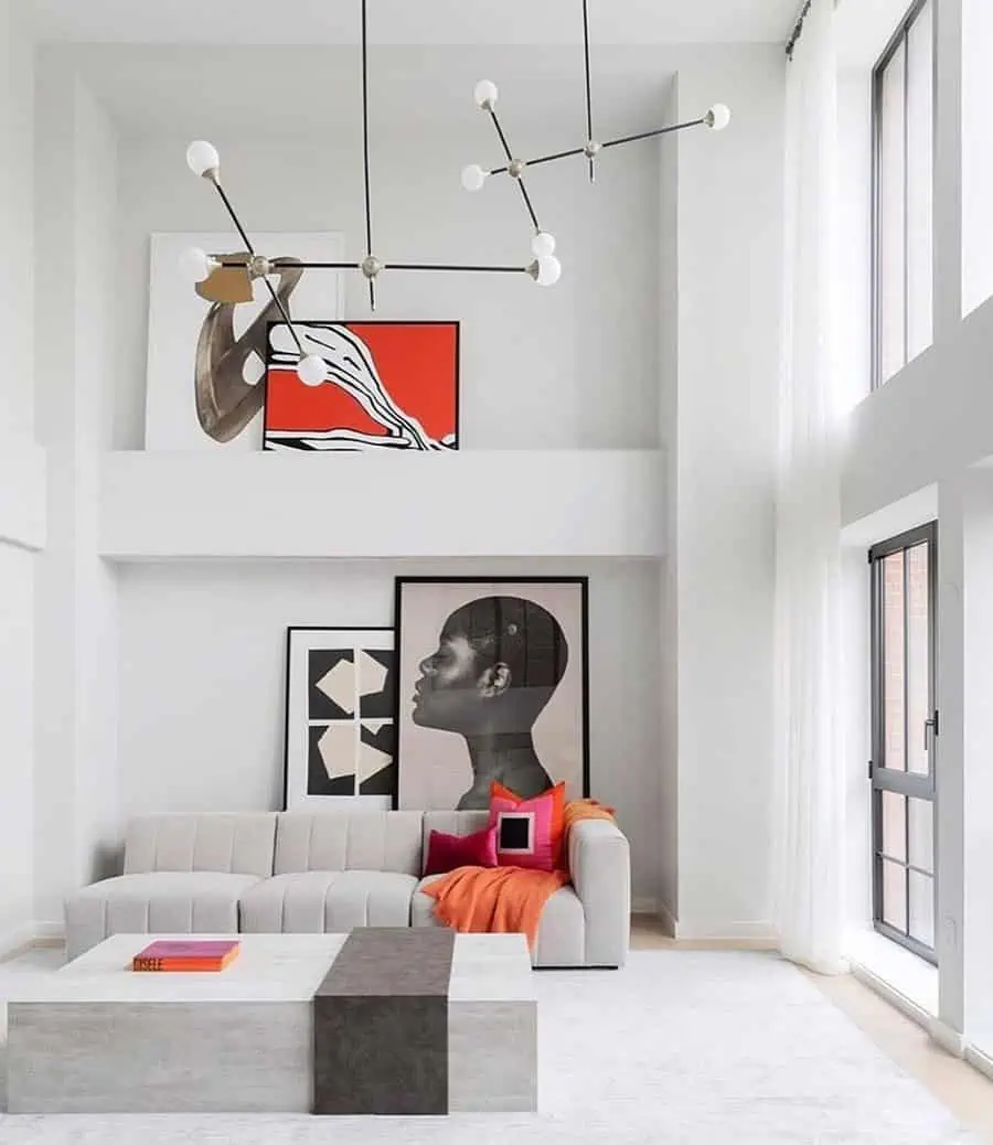 Contemporary living room with modern art, grey sectional sofa, geometric coffee table, and tall windows.