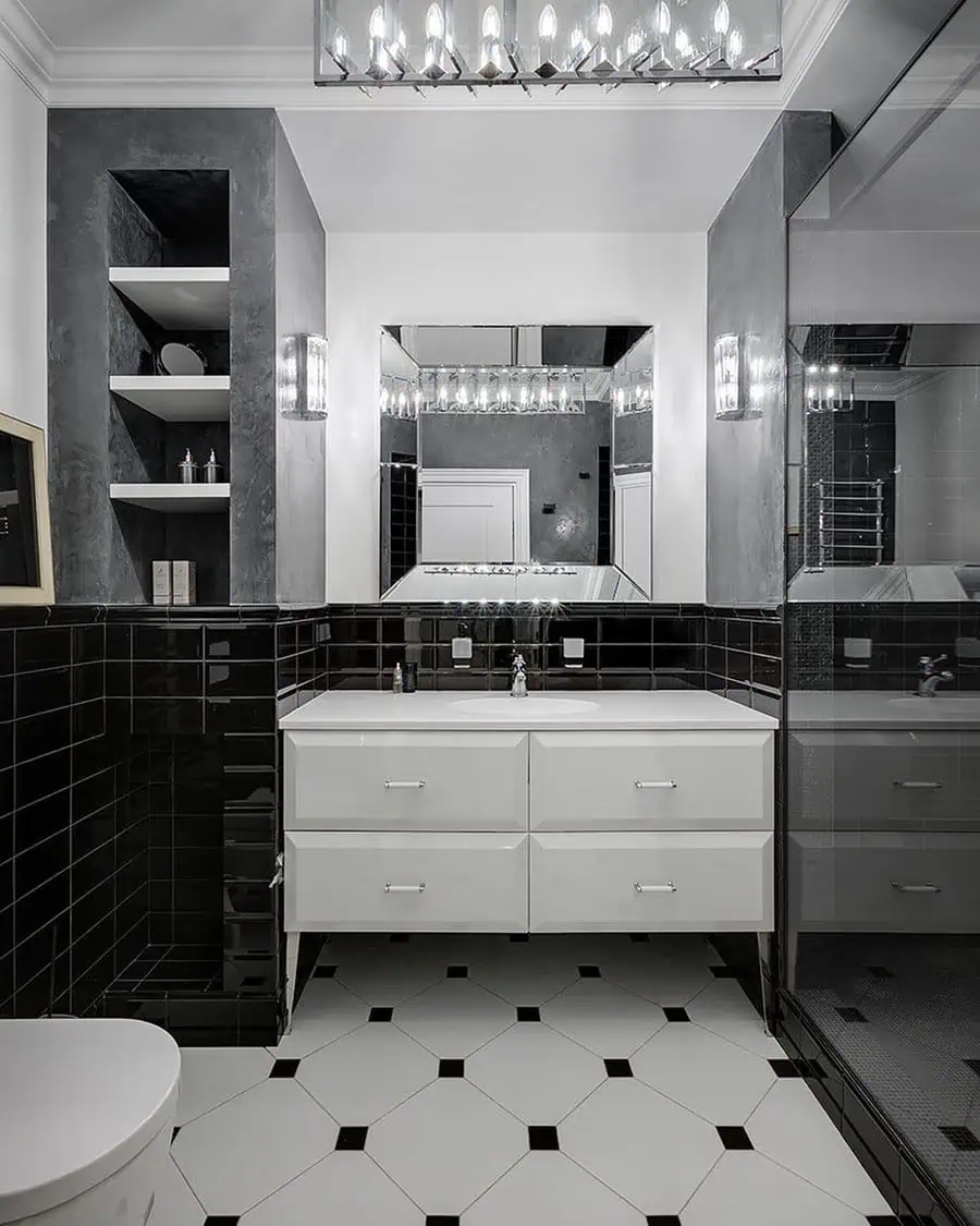 Monochrome Art Deco bathroom with black tiles, white vanity, geometric flooring, and mirrored lighting fixtures.