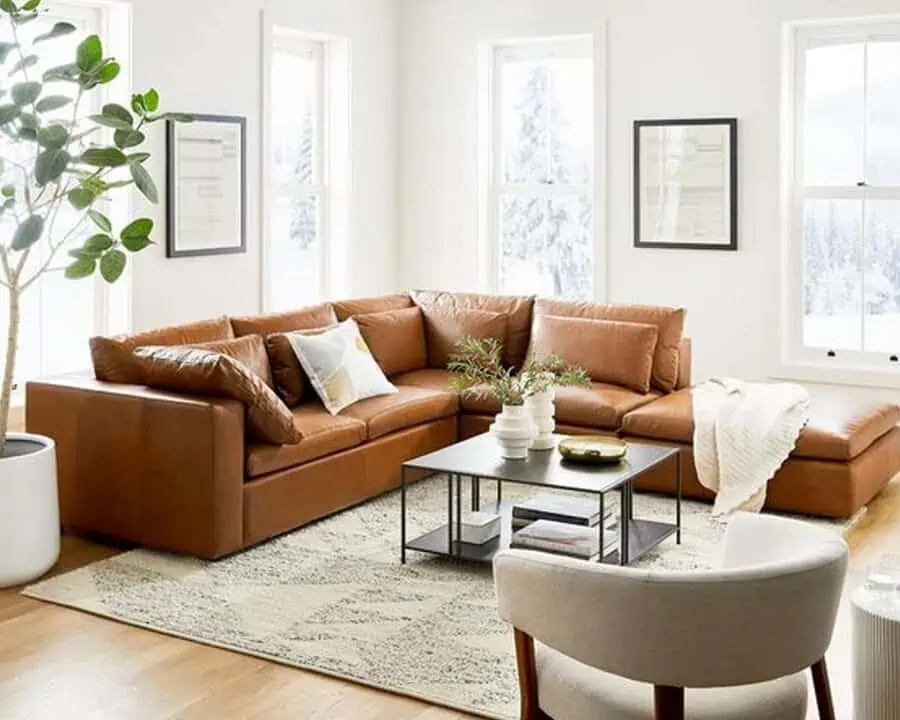 Spacious living room with a large leather sectional, coffee table, and greenery by the windows.