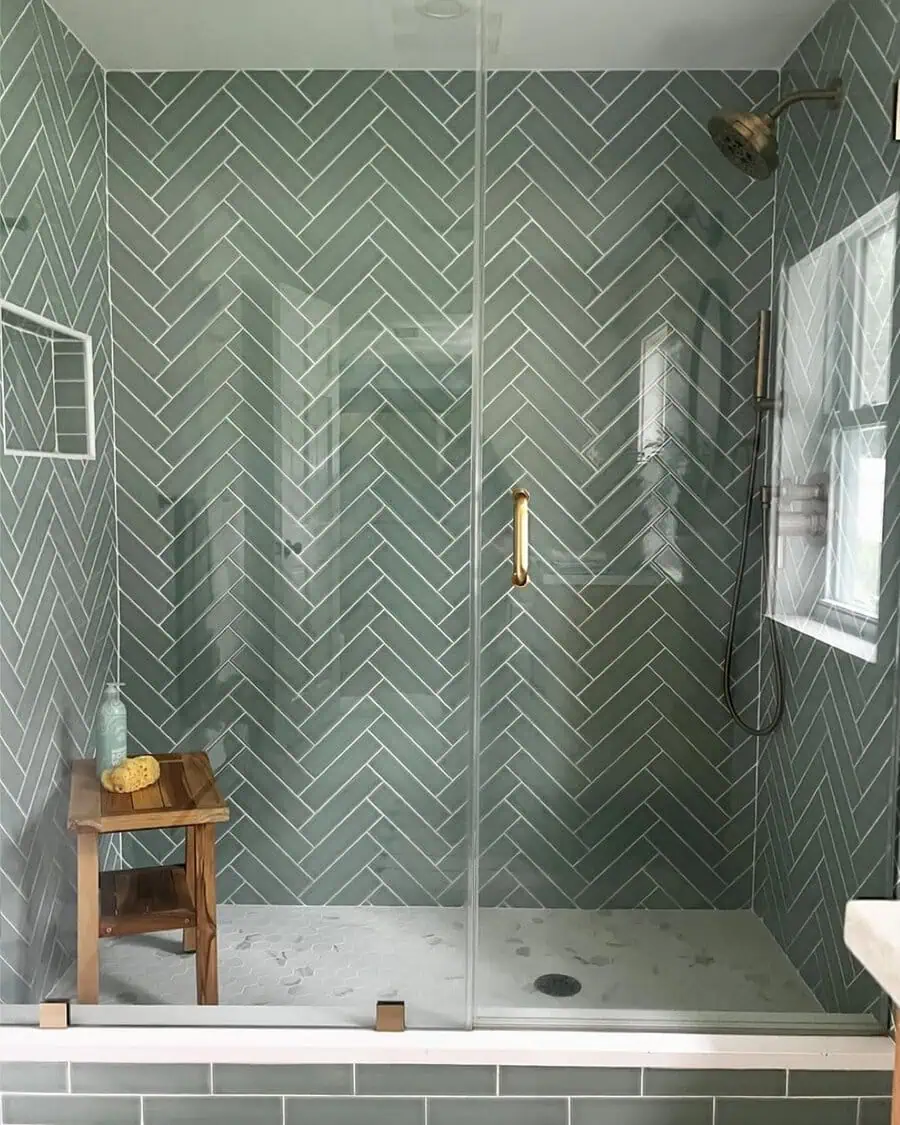 Shower with green herringbone tiles, brass fixtures, and wooden bench for spa essentials.