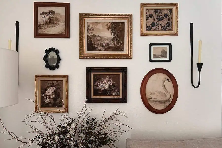 Rustic gallery wall with wood-framed vintage artwork and candle sconces for a cozy aesthetic.