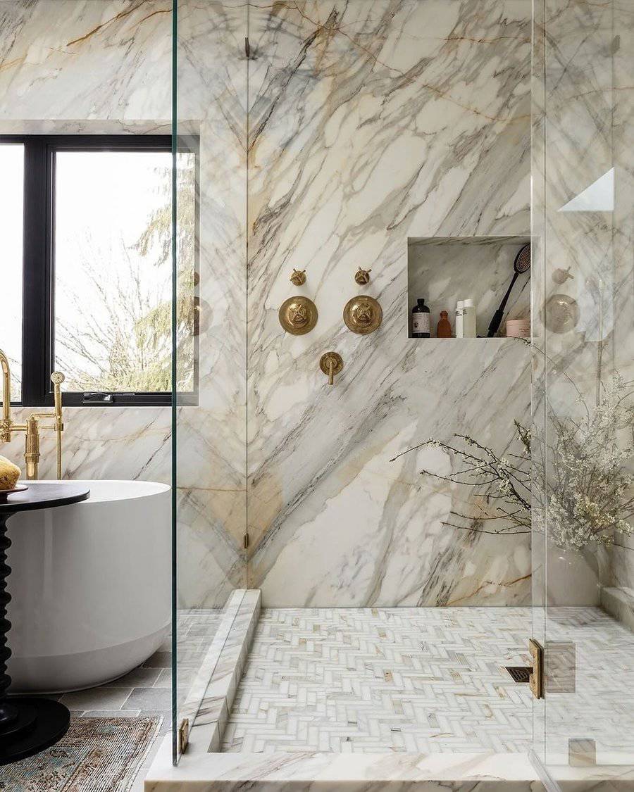 Shower room with marble walls, glass enclosure, and contemporary gold fixtures and bathtub.