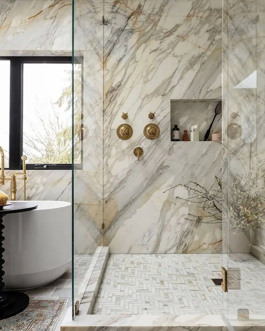 Shower room with marble walls, glass enclosure, and contemporary gold fixtures and bathtub.