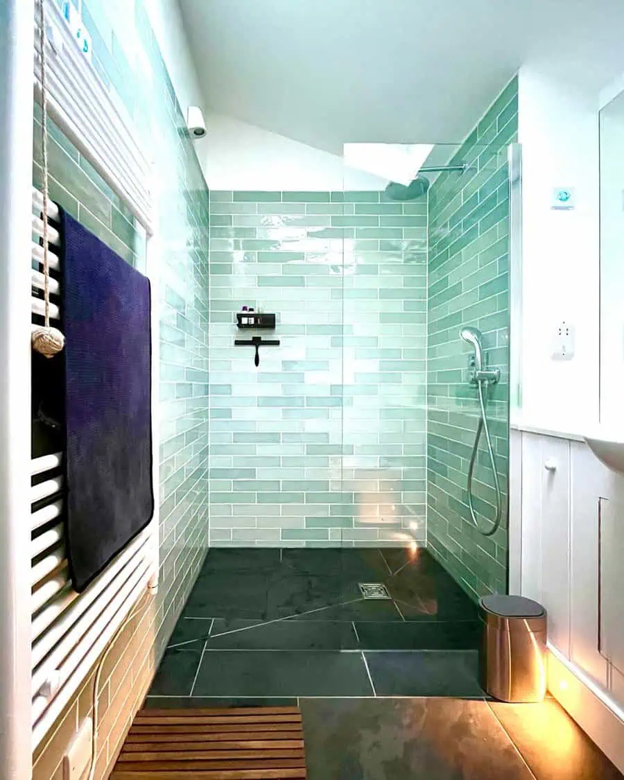 Shower with glossy mint subway tiles, black slate floor, and a heated towel rail.