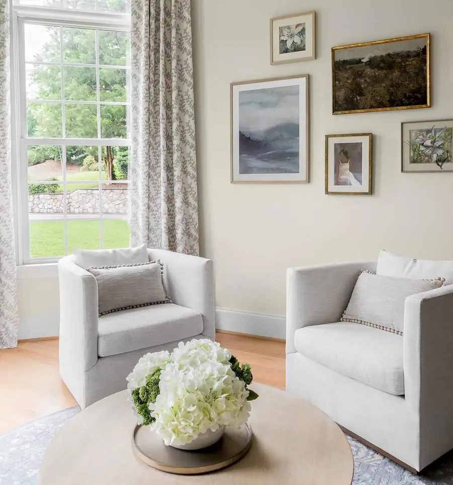 Small gallery wall with serene artwork and cozy armchairs in a bright sitting area.