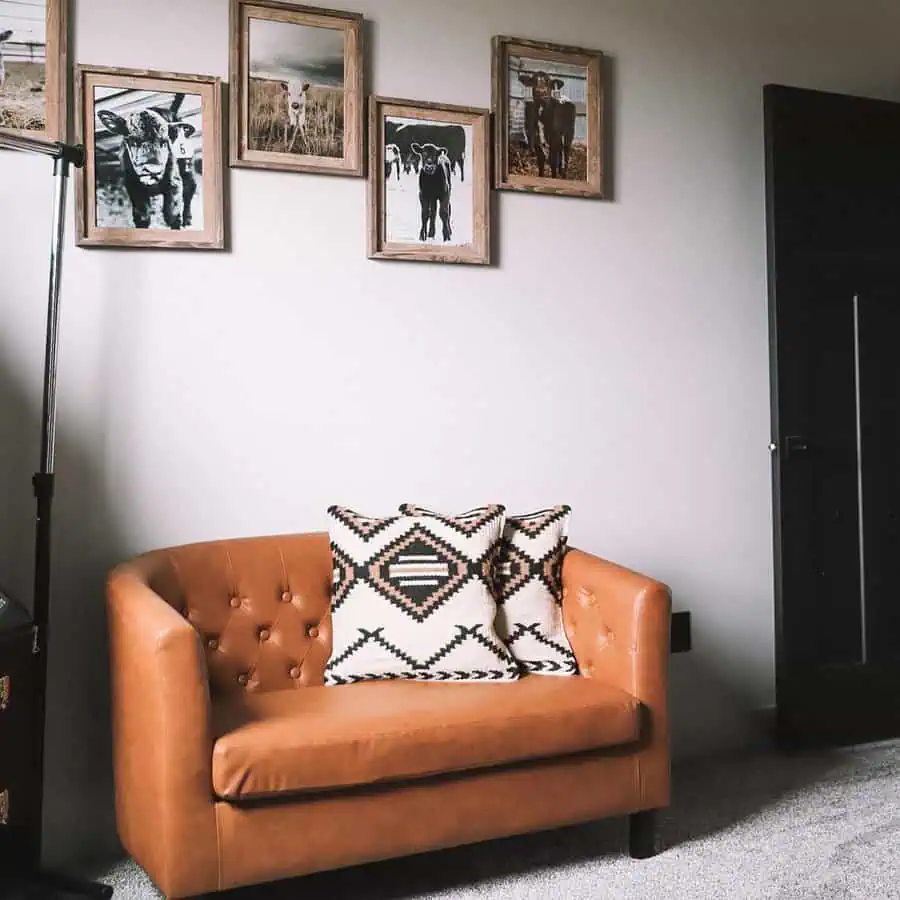 Brown leather loveseat with geometric-patterned pillows and framed cow-themed wall art.