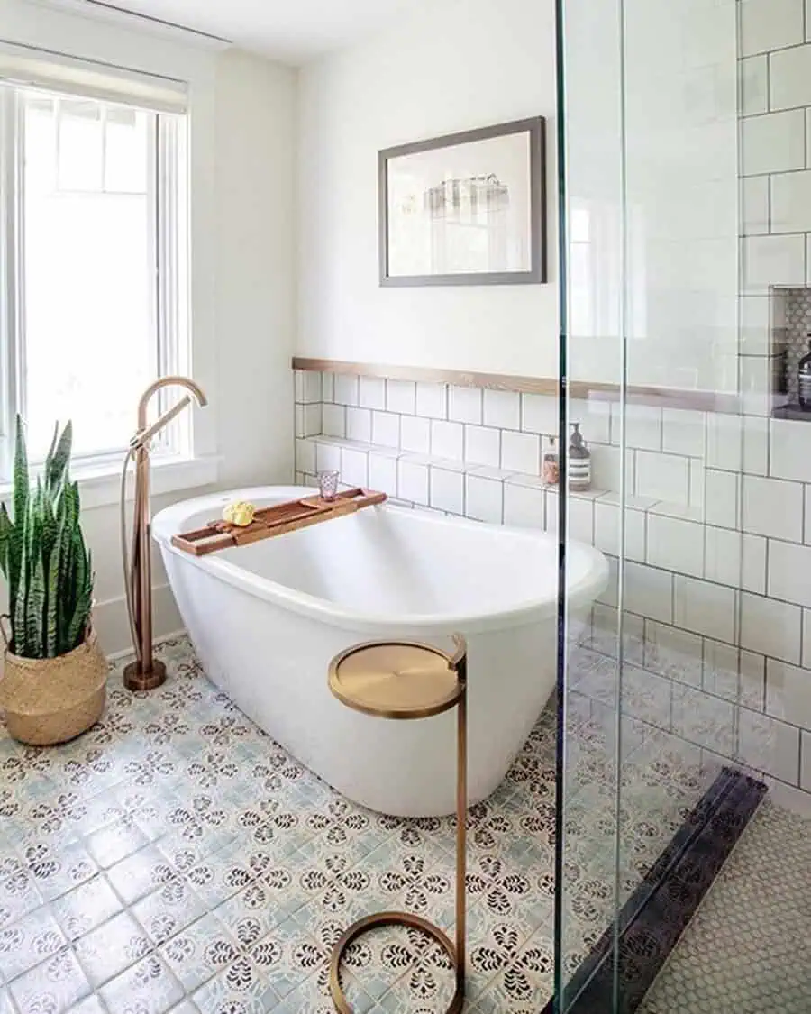 Freestanding bathtub with gold fixtures and a snake plant in a serene, tiled bathroom.