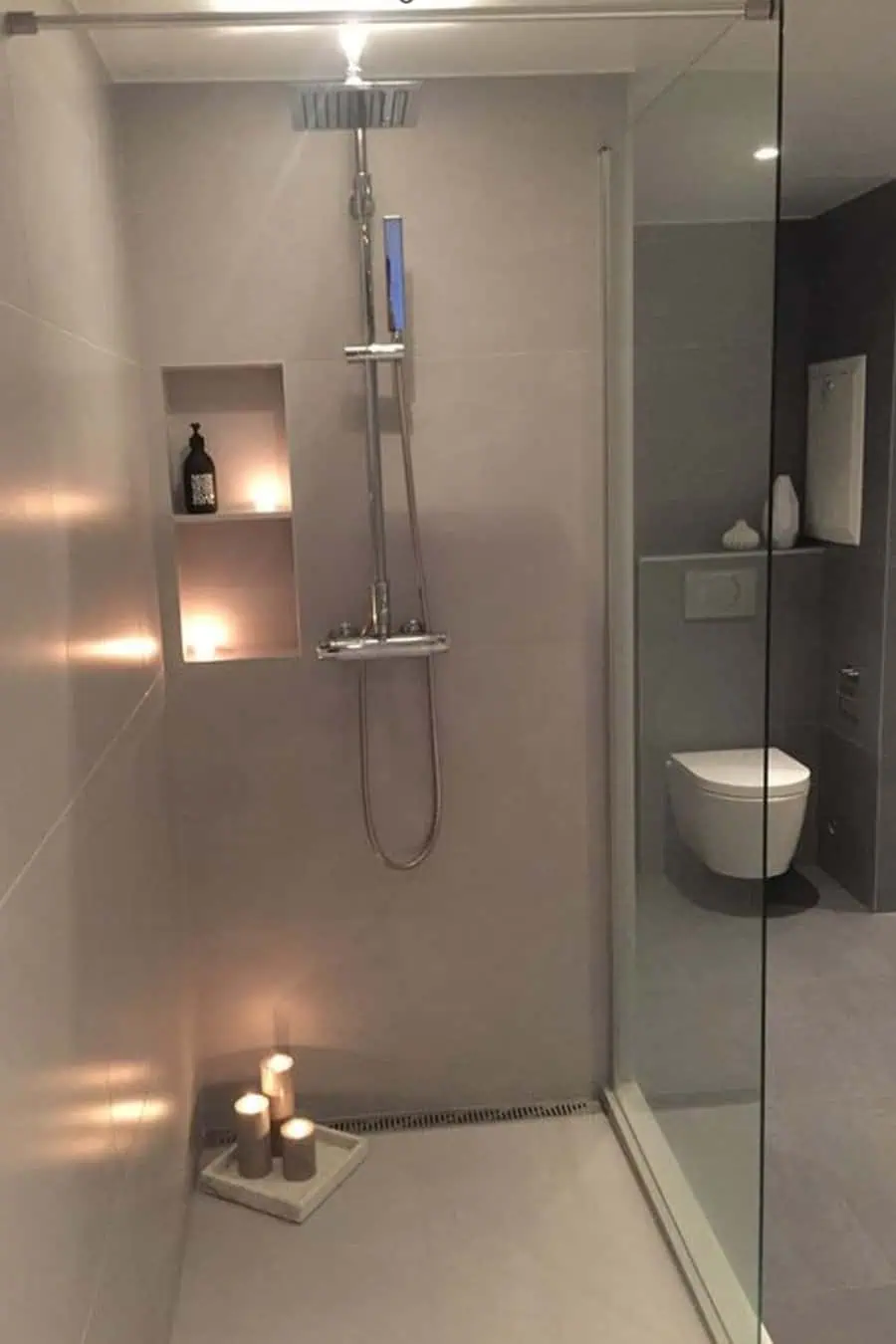 Stylish walk-in shower with gray tiles, recessed shelf, candles, and rainfall showerhead.