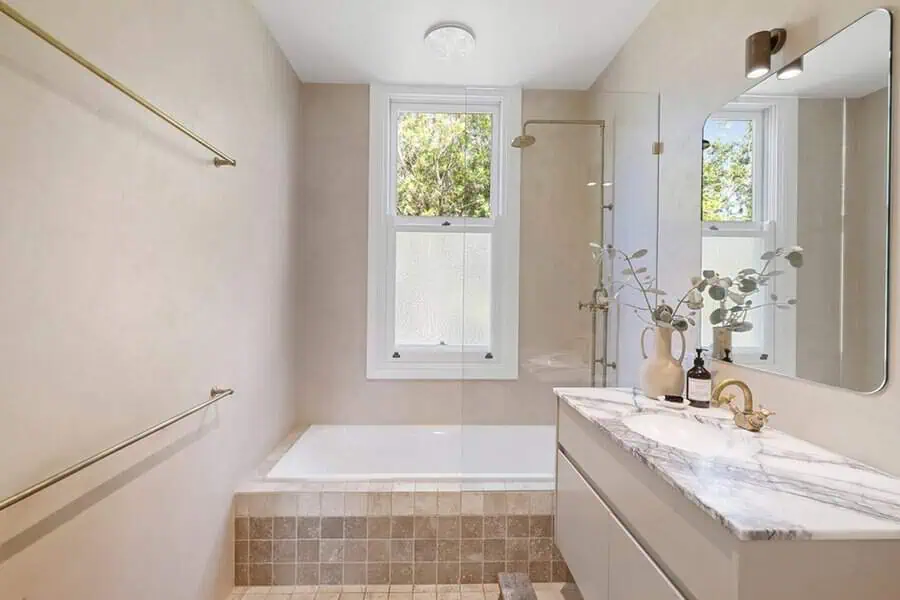 Timeless shower room with a neutral palette, marble countertop, brass fixtures, and a built-in bathtub with a glass partition.