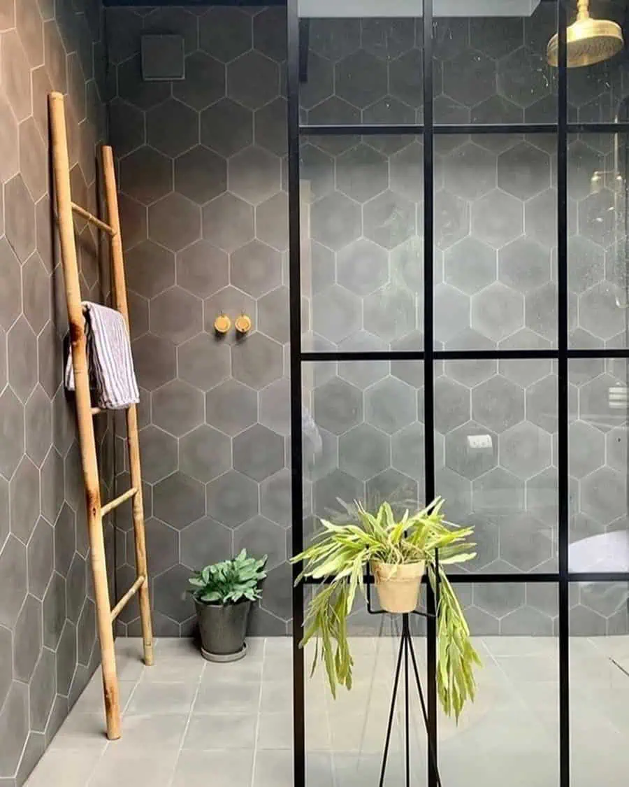 Glass shower with hexagonal tiles, wooden towel ladder, and potted plants for natural decor.