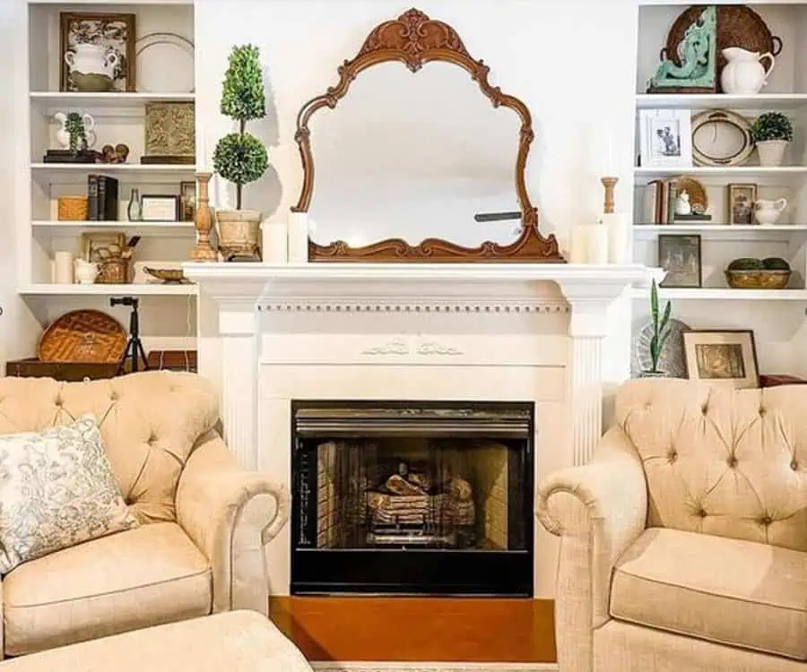 Traditional fireplace with an ornate mirror, decorative shelves, and cozy seating.