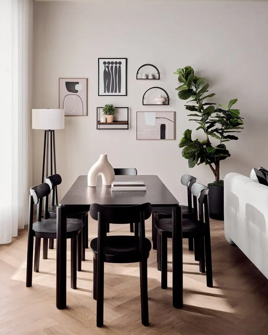 Minimalist gallery wall with abstract art pieces and floating shelves in a sleek dining room featuring black chairs, a modern black table, and a large green plant.