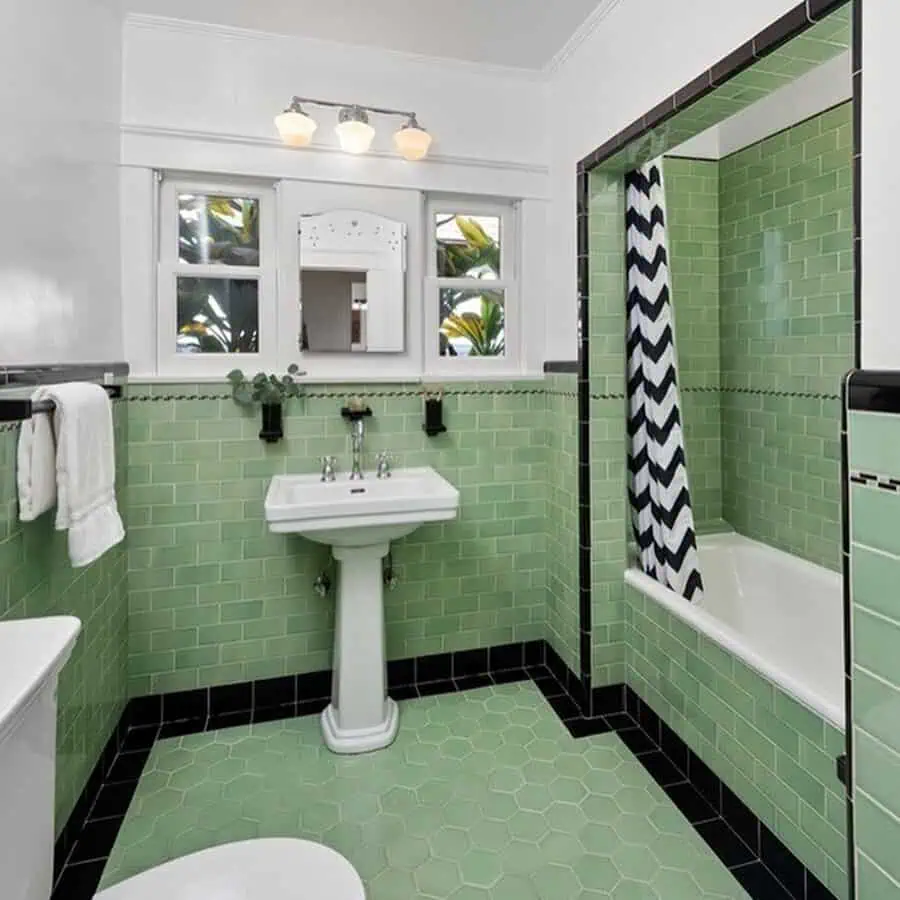 Vintage Art Deco bathroom with green subway tiles, hexagon floor tiles, pedestal sink, and bathtub.