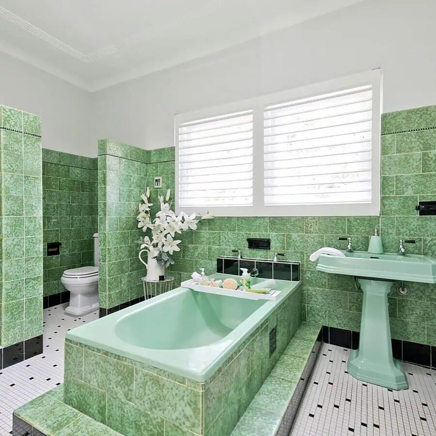 Vintage Art Deco bathroom with mint green tiles, bathtub, pedestal sink, and white accents.