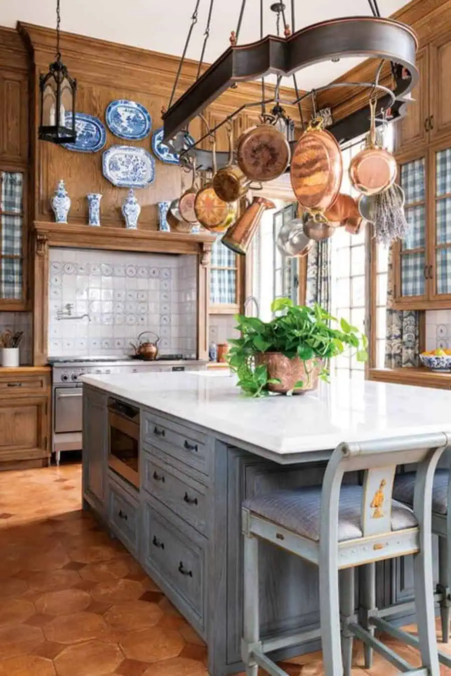 A rustic kitchen with wood cabinetry, copper pots hanging above a large island, and decorative blue and white porcelain accents.