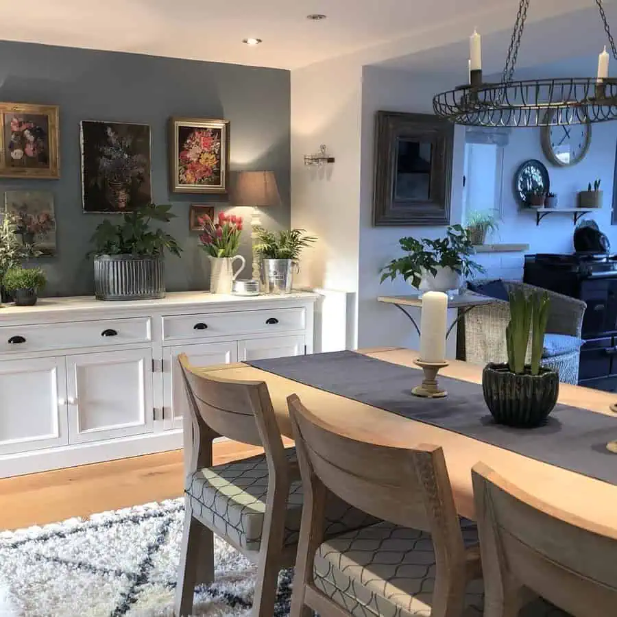 Dining room with vintage gallery wall, wooden table, and potted plants for a cozy ambiance.