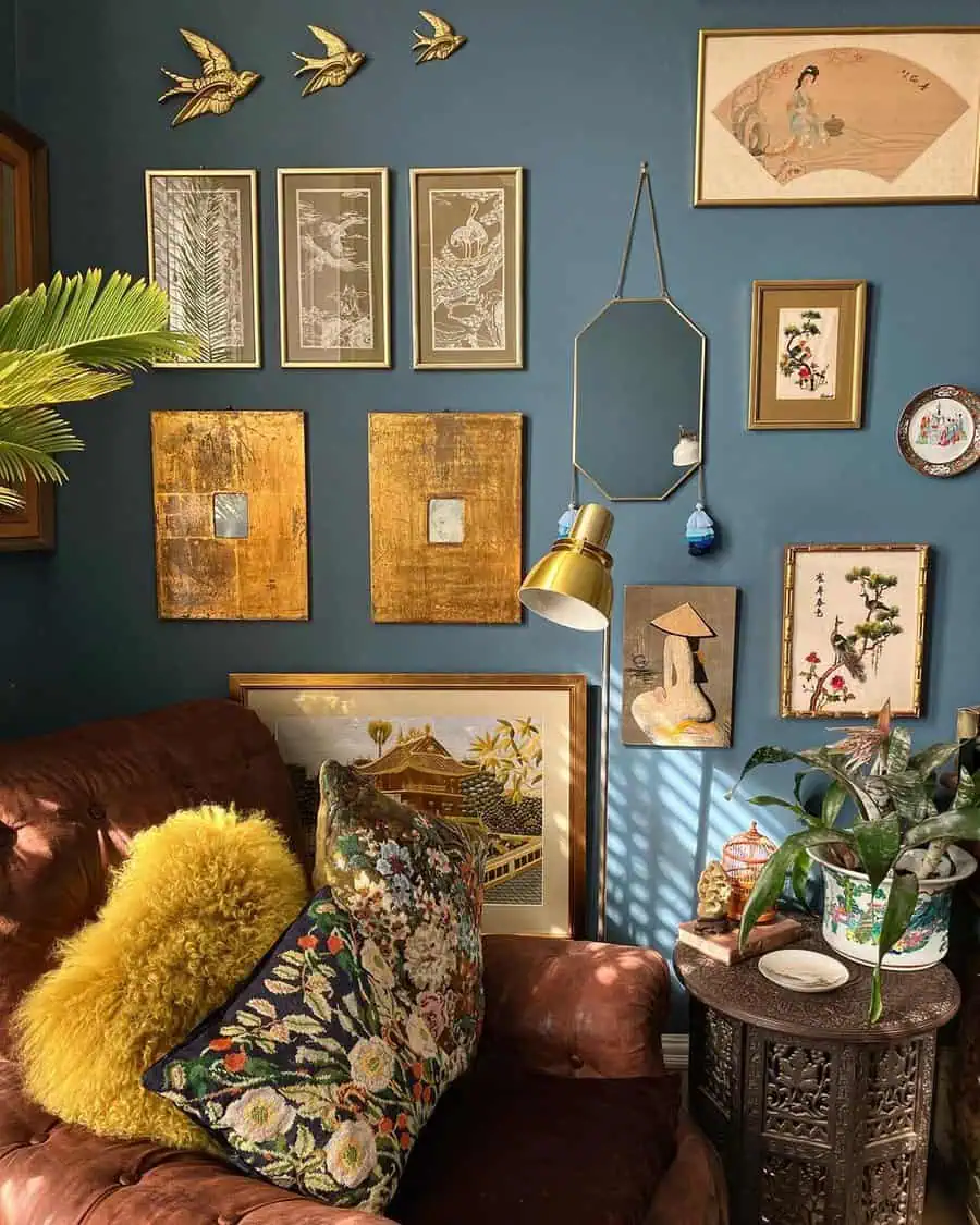 Vintage gallery wall with eclectic art, tufted chair, and floral pillows in cozy corner.