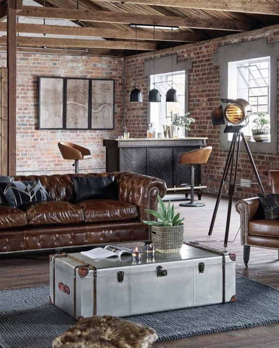 Industrial-style living room with vintage leather seating, exposed brick walls, and a metal trunk coffee table.