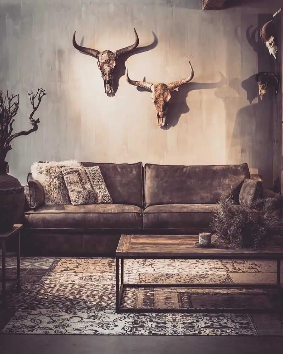 Rustic living room with dark brown leather sofa, mounted skull decor, and wooden coffee table with vintage charm.