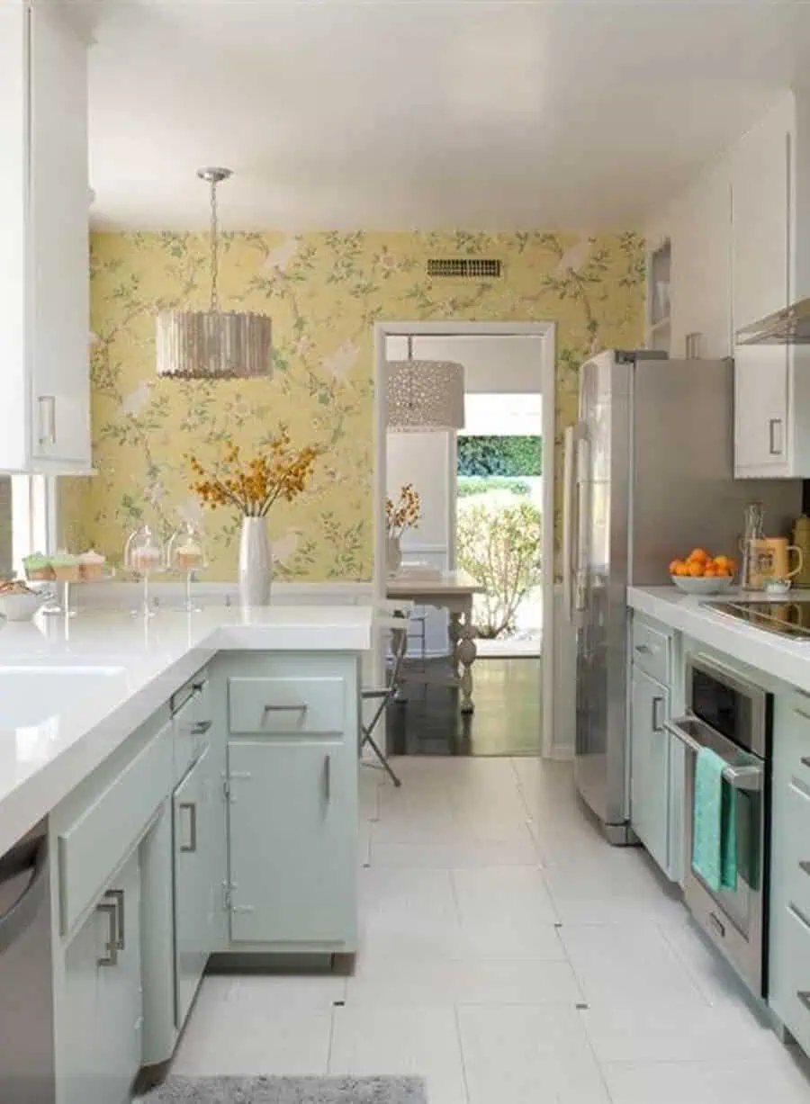 1950s kitchen with pastel cabinets, bold yellow floral wallpaper, and stainless steel appliances.