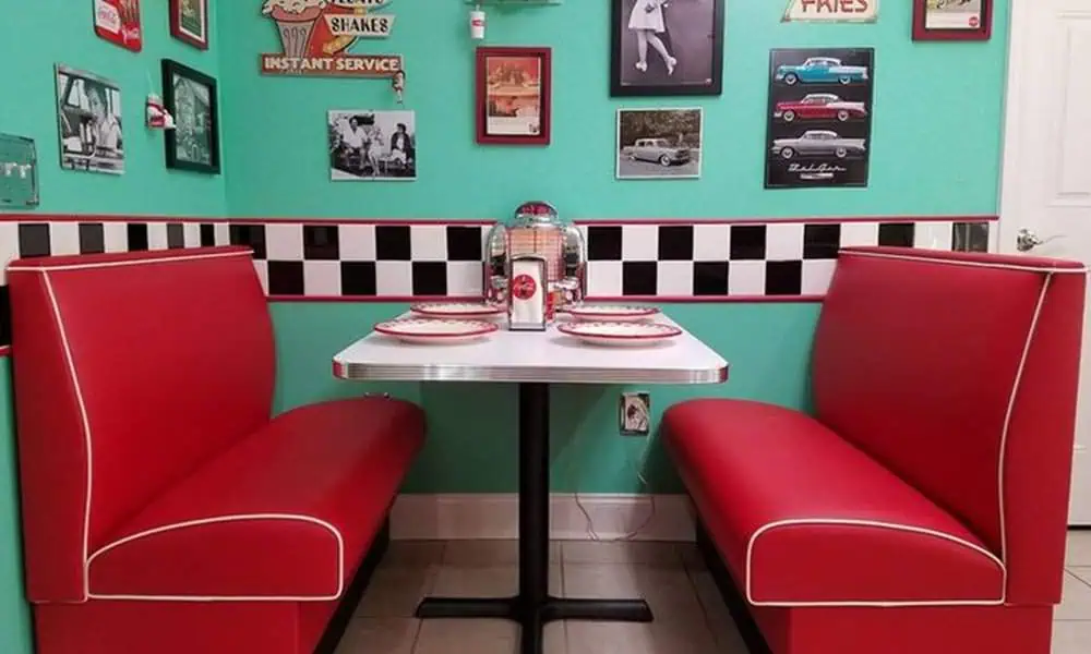 1950s retro diner booth with red seating, checkered wall, and vintage decor accents.